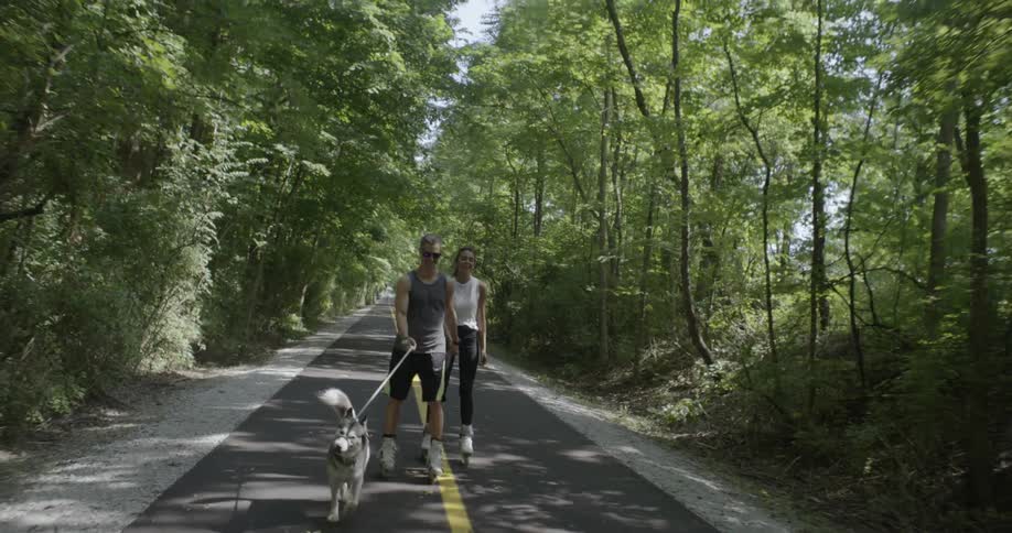 Man and woman rollerblade while walking a dog