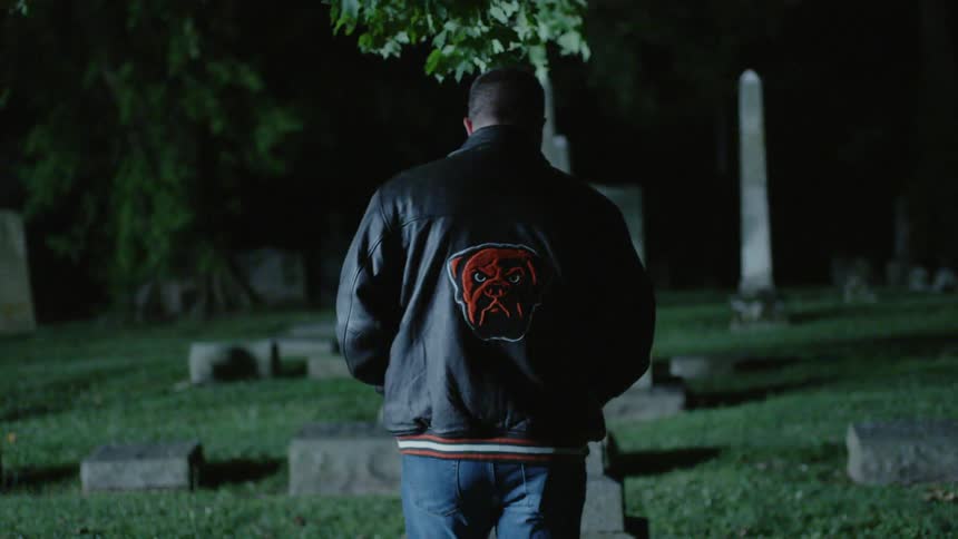 A man in a leather jacket walks through a graveyard