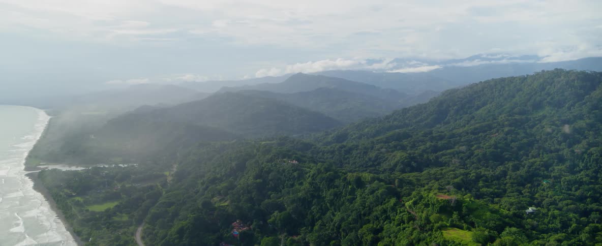 Clouds are hanging above a mountain range and coastline on a foggy day
