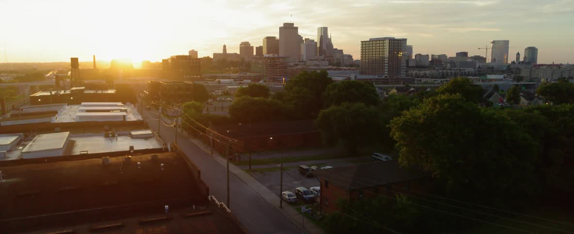 Telephone wires and poles line a street while the sun sets on a city skyline