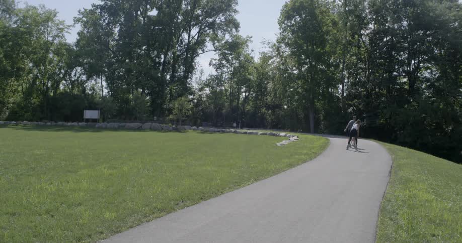 A couple are skating around a park with their dog on a leash