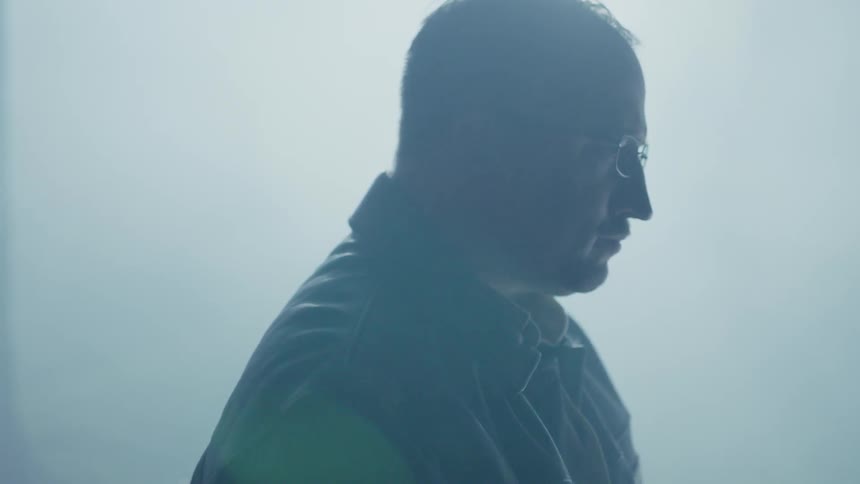 A man in glasses stands in a dim room