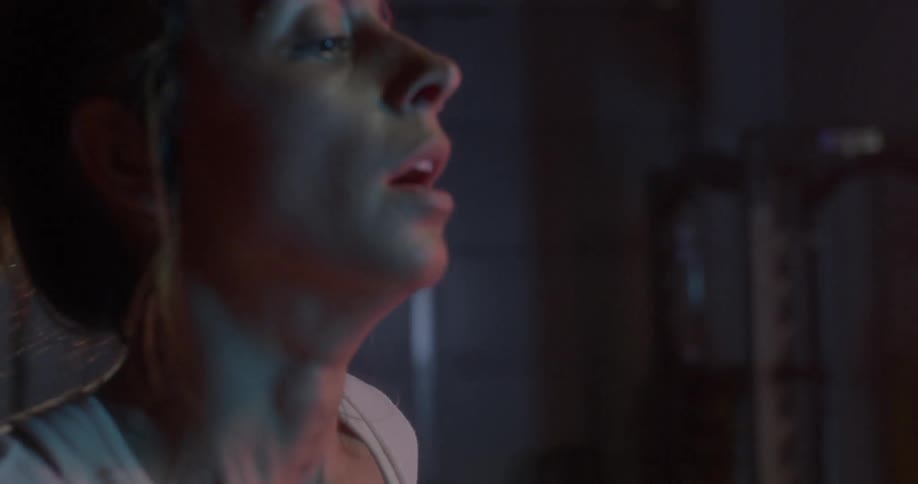 A woman catches her breath in a dimly lit gym