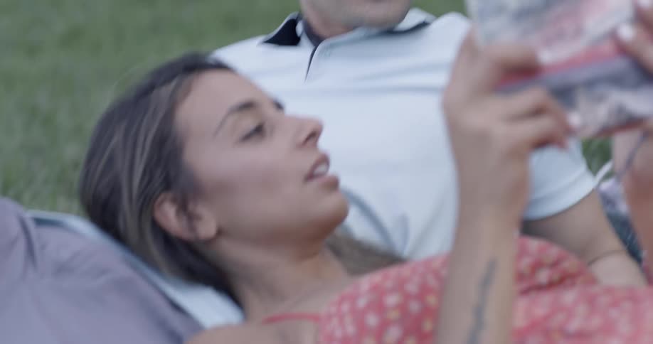 A man and woman relax in a park and read a book