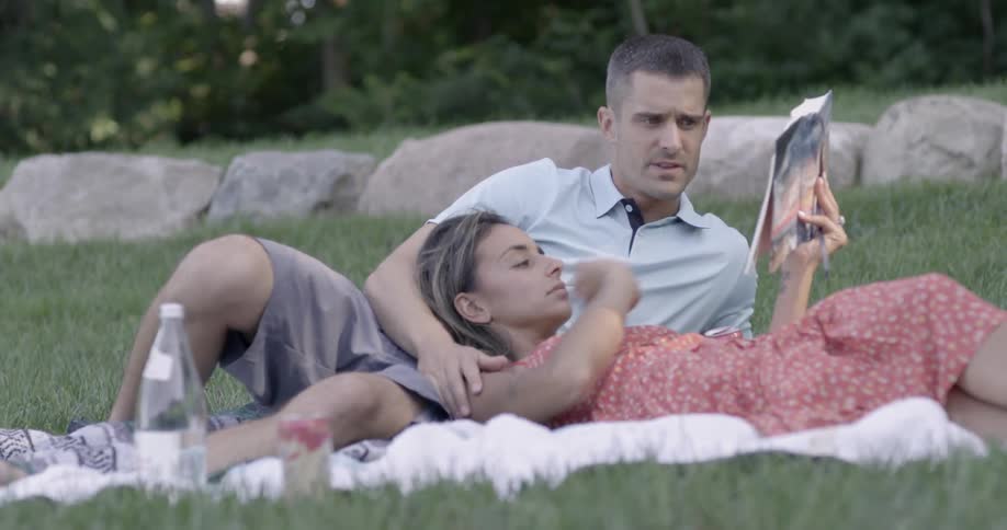 A man and woman relax in a park and read a book