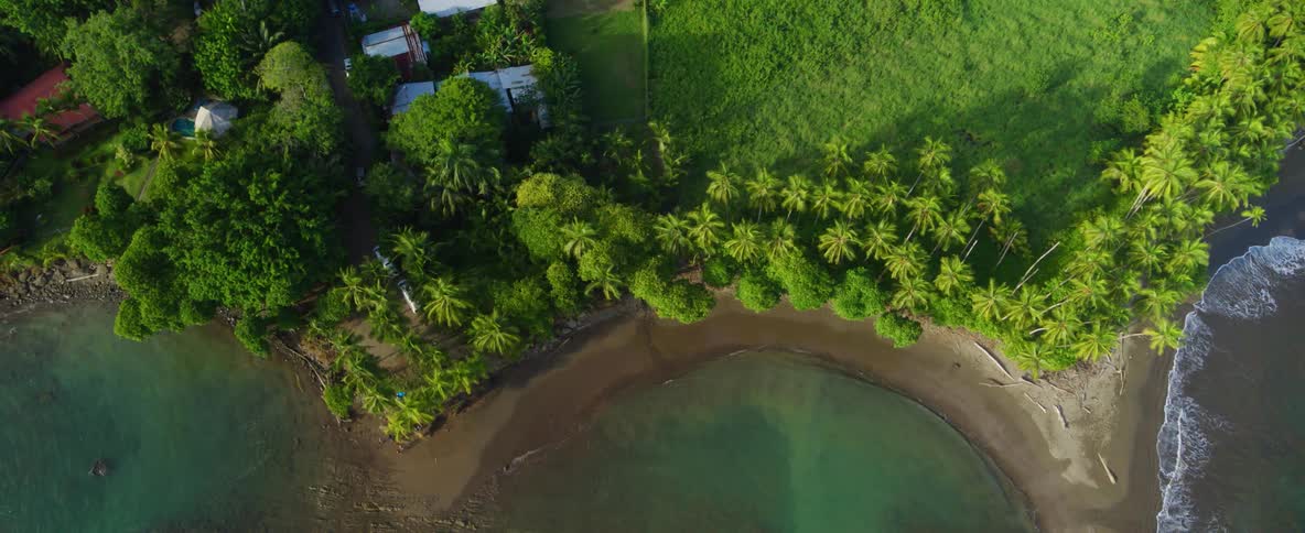 A overhead shot of a lush green village next to a beach