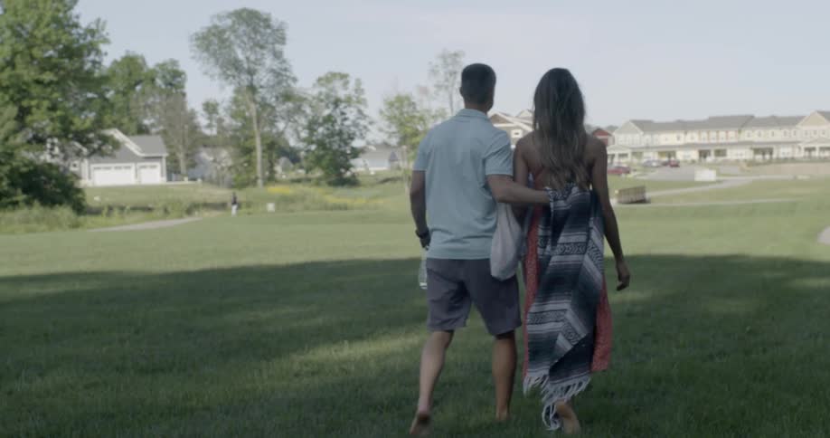 A man carries a blanket as he walks with a woman in a park on a sunny day