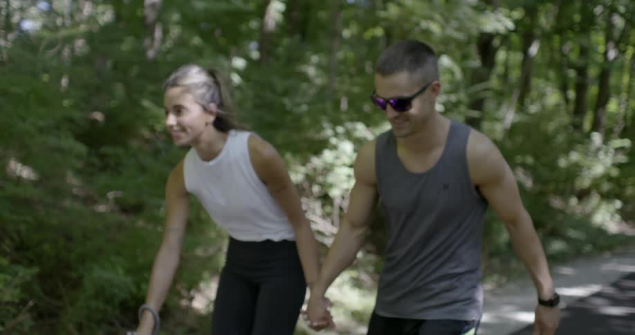 A man and woman are skating through the forest holding hands