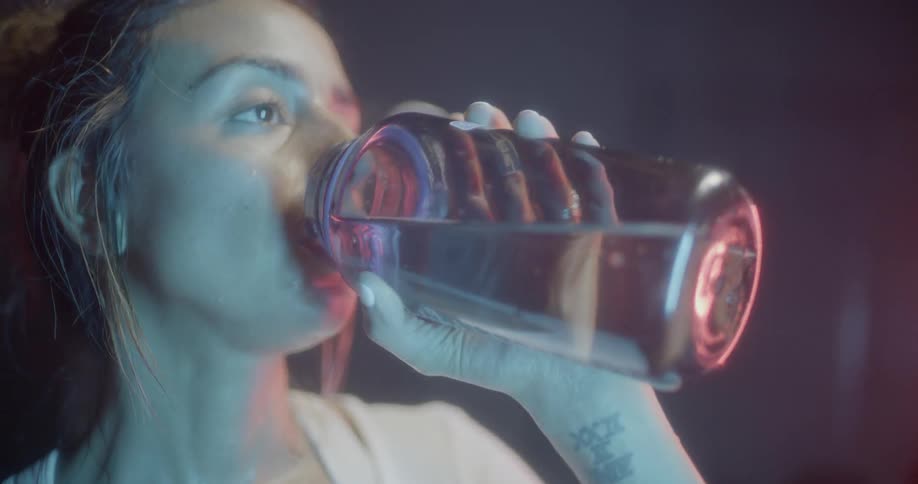 A woman opens a bottle of water and takes a drink in the gym