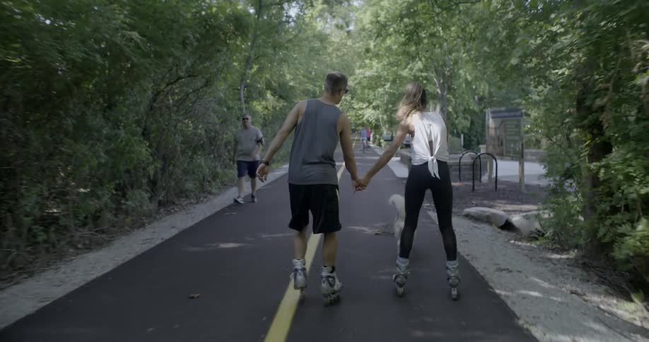 A couple and their dog are skating down a path