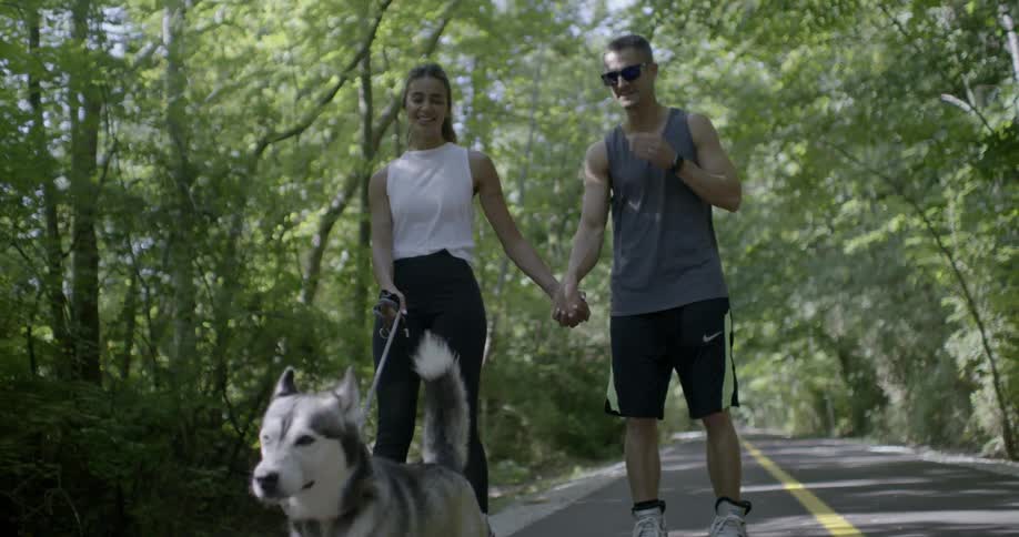 Two people skate while walking their dog
