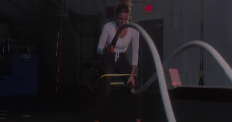 A woman is waving large ropes in the gym and then drops them when shes out of breath
