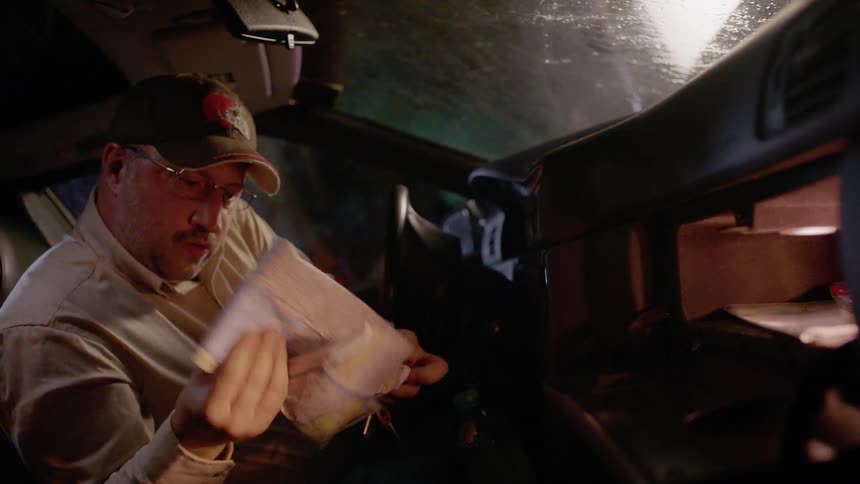 A man is searching through a car's glove compartment at night