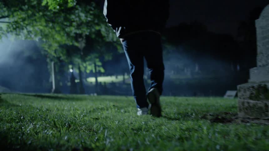 A man is walking through a cemetery at night