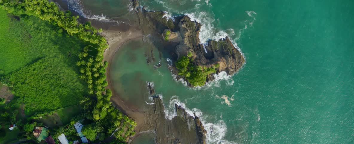 Waves crash over rocks and onto a beach in a lagoon during the day