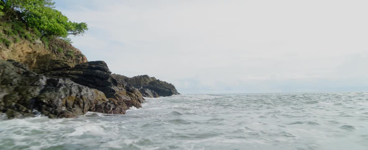 Waves are rolling over rocks and splashing against the shoreline on a cloudy day