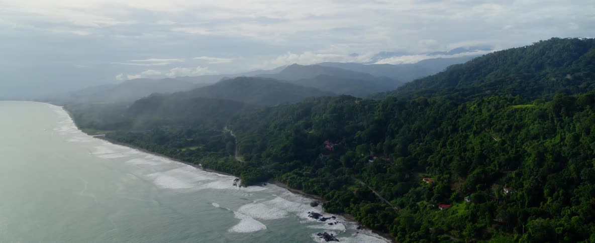 Waves are rolling ashore at the base of mountains during the day