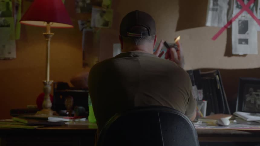 A man flicks a cigarette lighter as he sits at a desk in a room