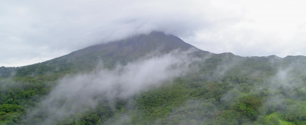 Clouds hang over tree tops and a mountain peak