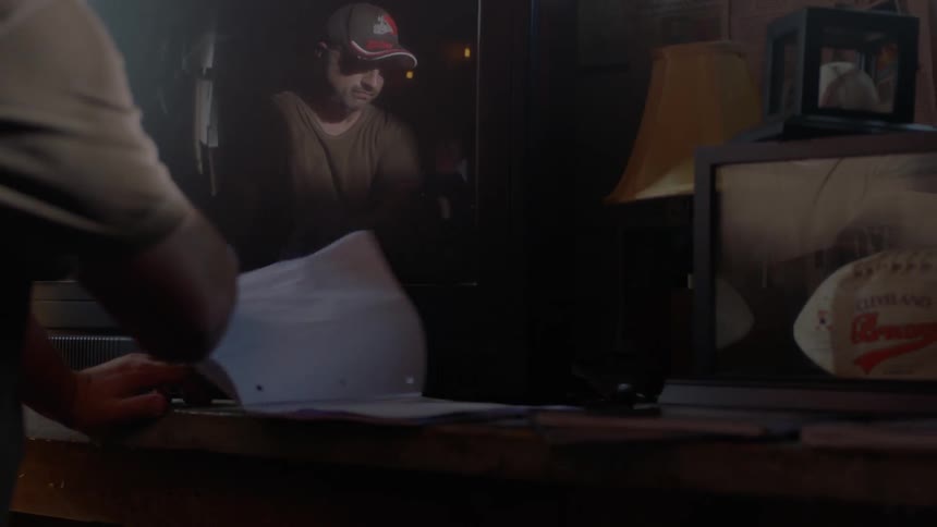 A man's image is reflected in a tv screen as he tosses papers around