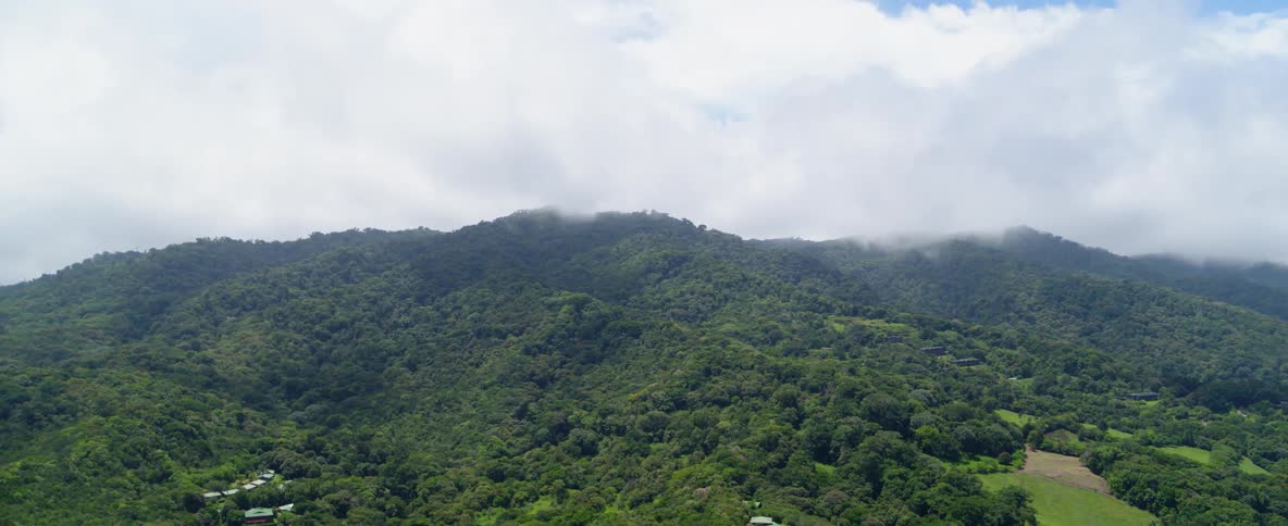 Clouds hang above a green tree covered mountain