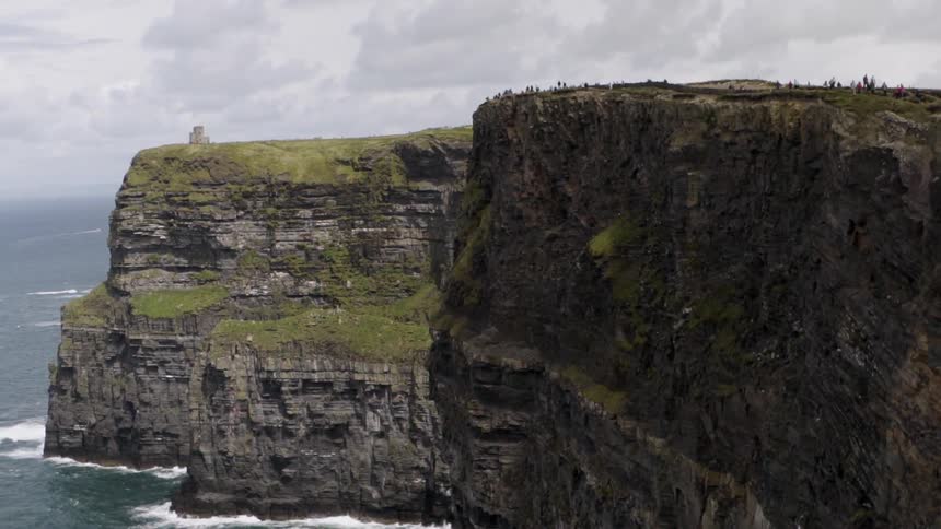 People look out onto the water from a large rock cliff