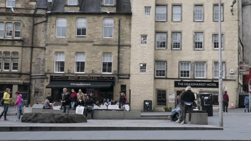 Cars drive on a city street with pedestrians walking on a sidewalk