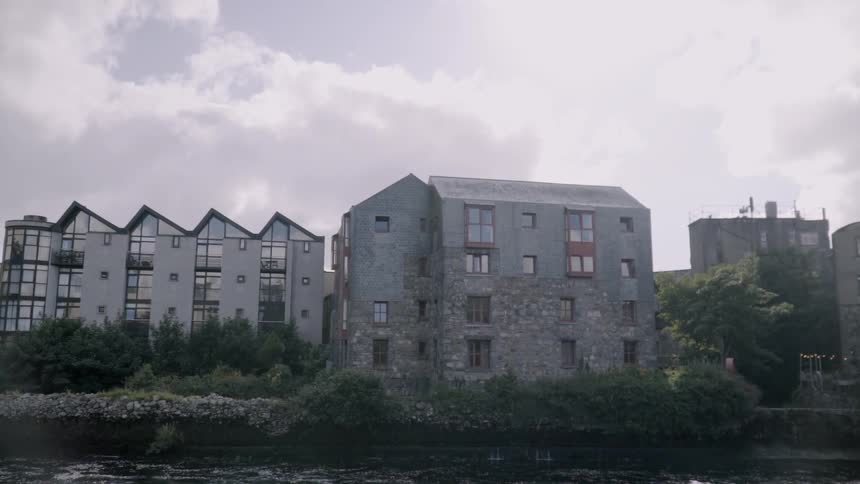 A river is running past several apartment buildings on a cloudy day