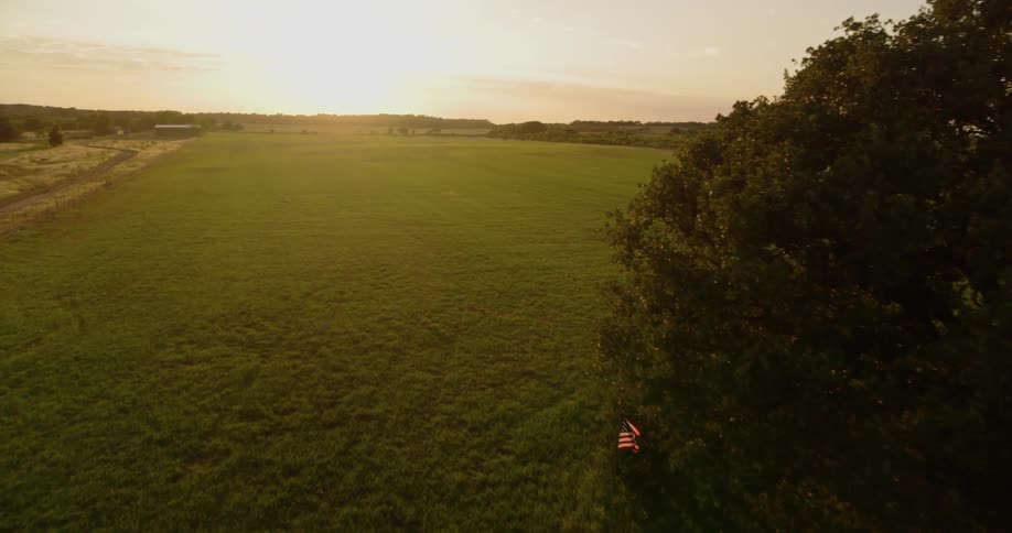 An american flag billows in a rural field at sunset