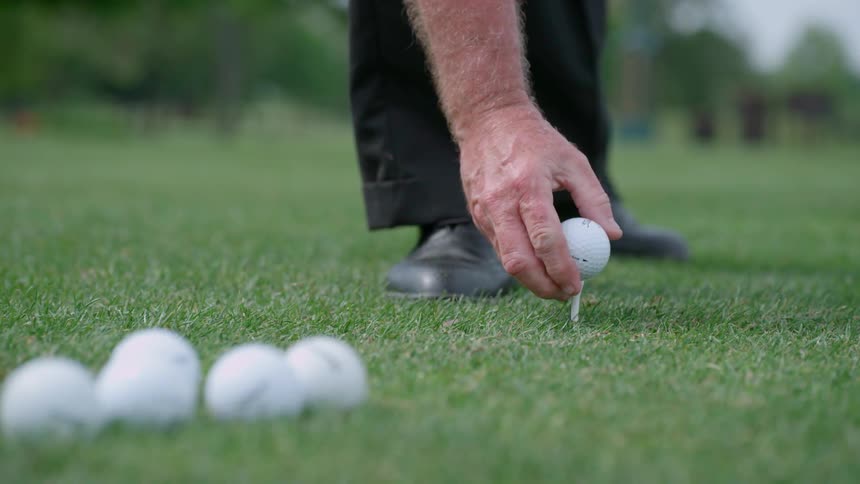 A man places a golf ball on a tee