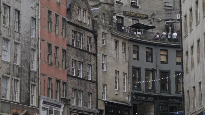 Large old stone buildings with people on one of the roofs is viewed from street level