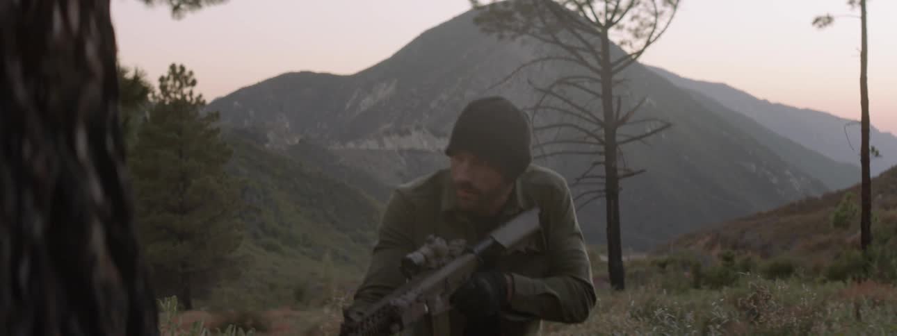A man is searching around the wilderness with a large rifle