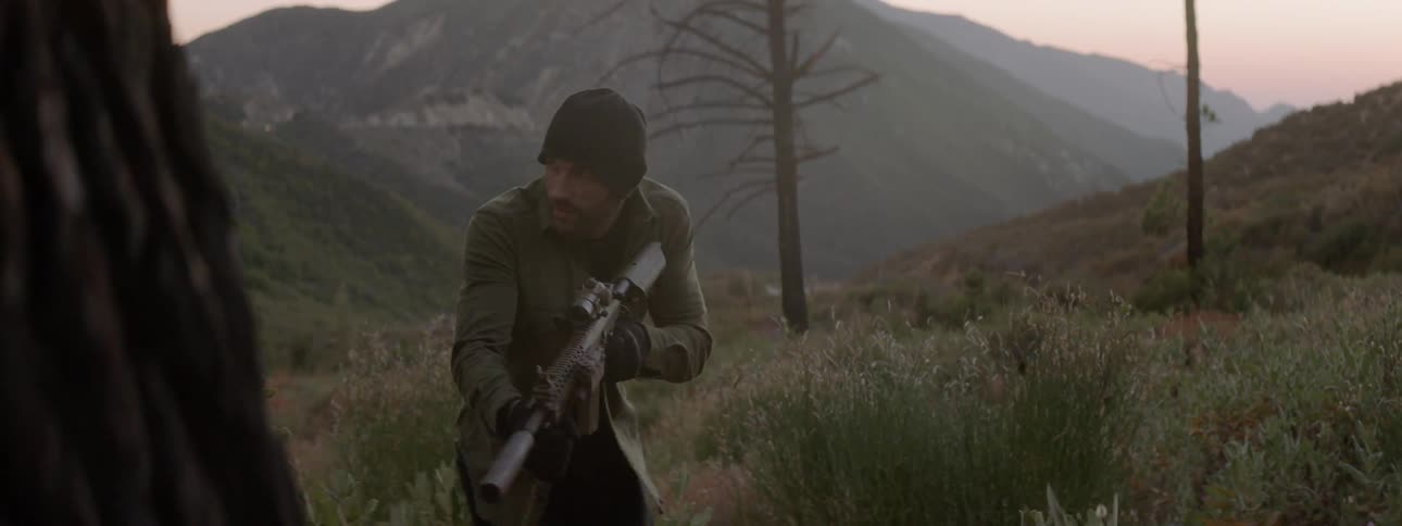 A man with a gun is slowly walking through the desert