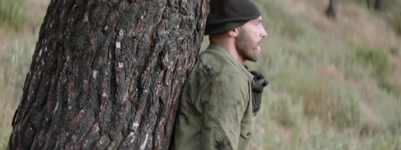 Man shoots a gun and hides behind a tree