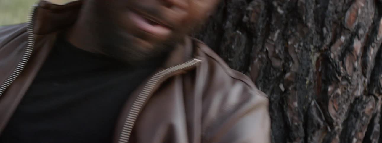 A man holding a rifle leans against a tree yelling