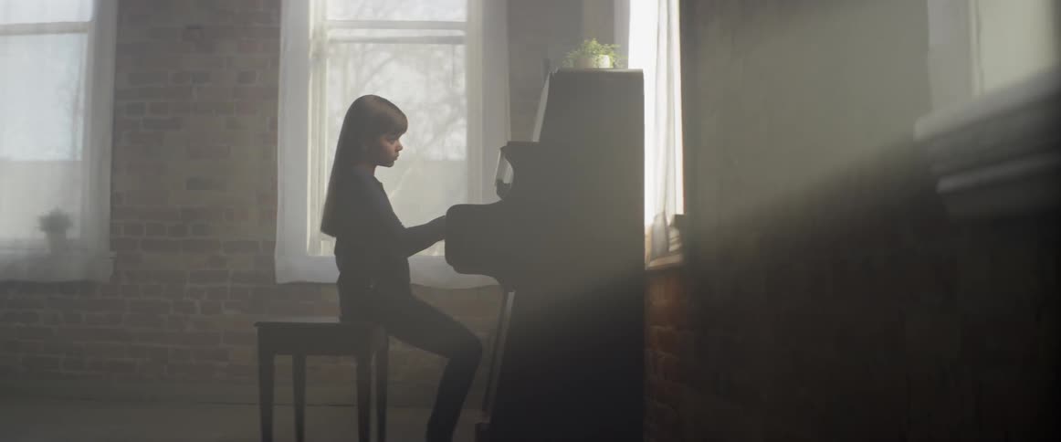 A girl is concentrating as she plays the piano during the day