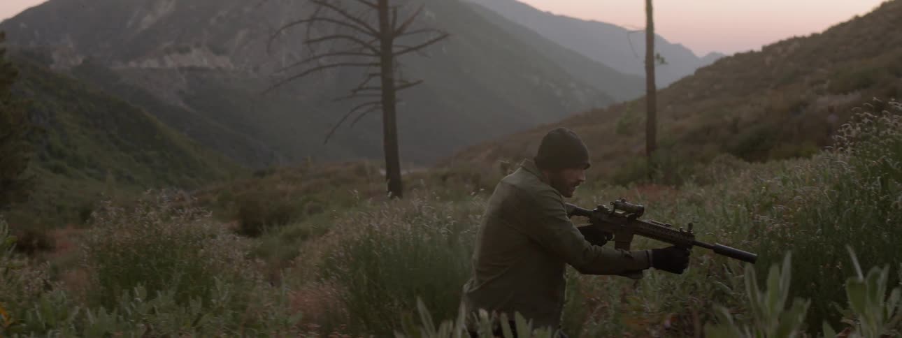 A man with an assault rifle is stalking something through the desert