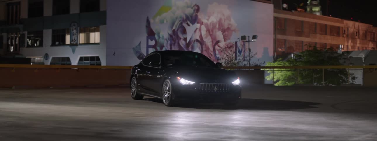A car sits parked with its headlights on in an empty parking lot at night