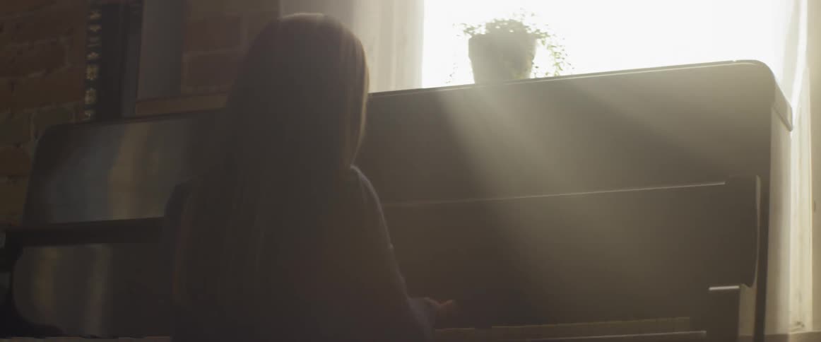 A child is playing the piano in front of a window