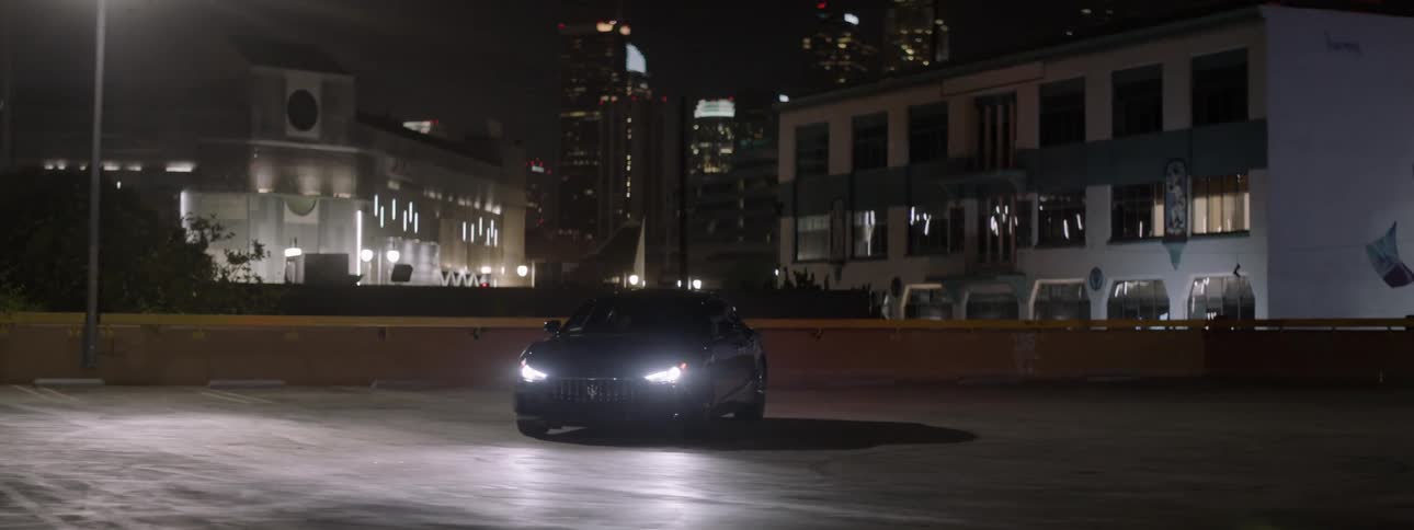 A car is sitting with its headlights on and the city in the background at night