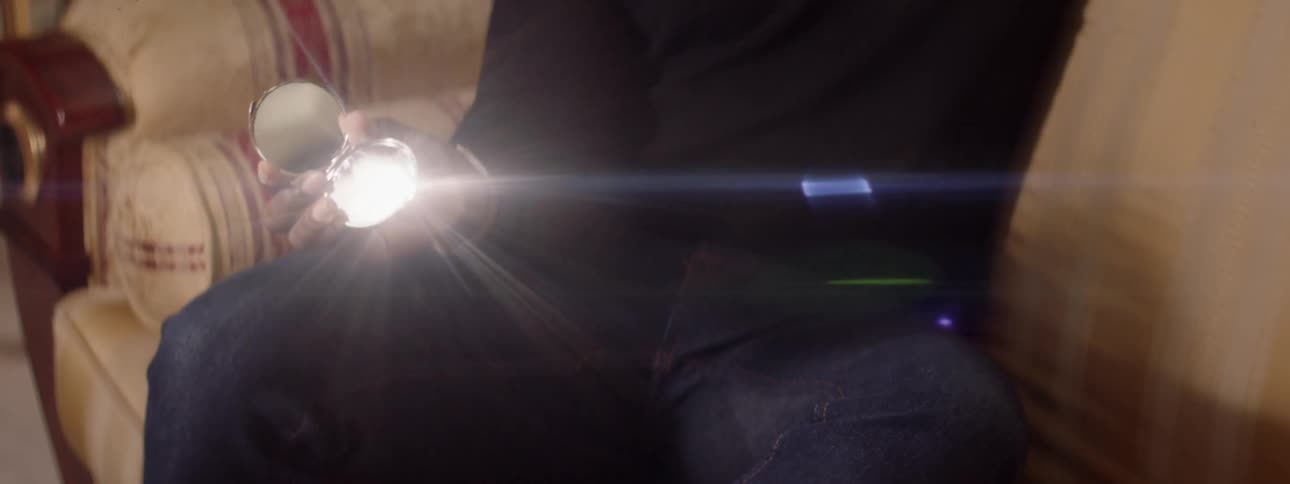 A man is sitting and reflecting sunlight in a mirror he is holding in his hand