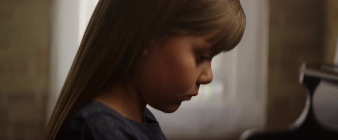 A girl is concentrating as she plays the piano during the day