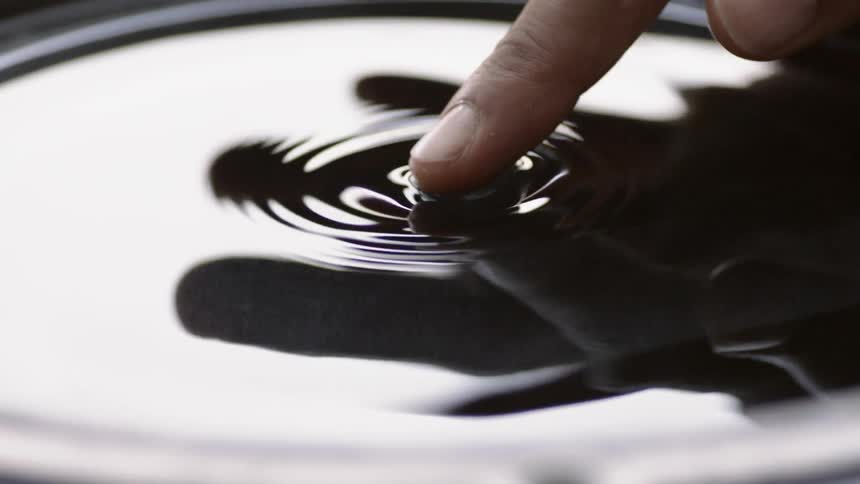 Finger pushing on a small air bubble on top of liquid