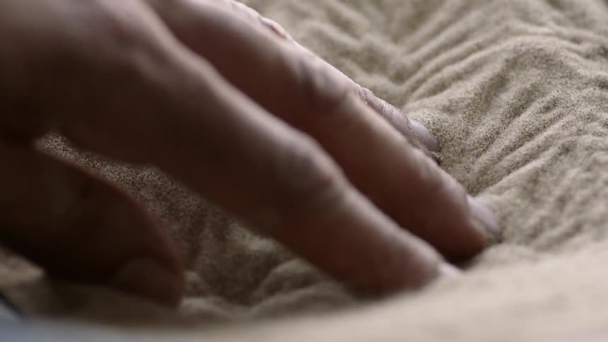 A man's fingers are feeling sand as it vibrates and moves