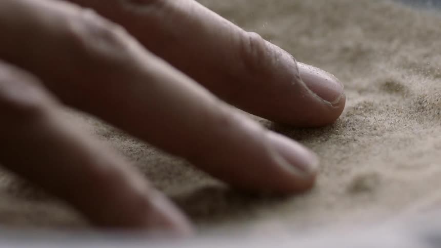 Fingers are touching sand as it is vibrating in a container