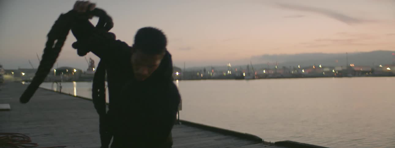 A man is gathering up a large rope on a dock