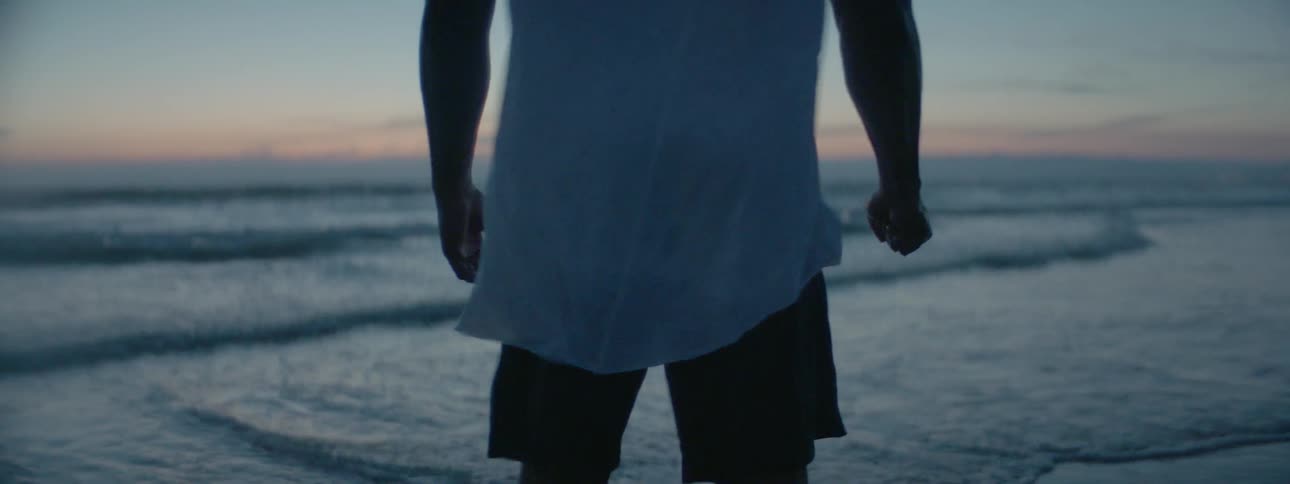 A man stands on the beach flexing his hands at dusk