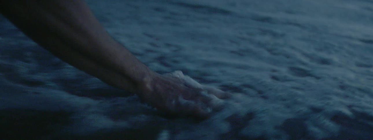 A person grabs a handful of sand from the water