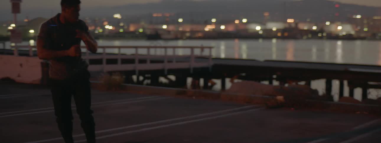 A man shadow boxes and kicks outside by the water