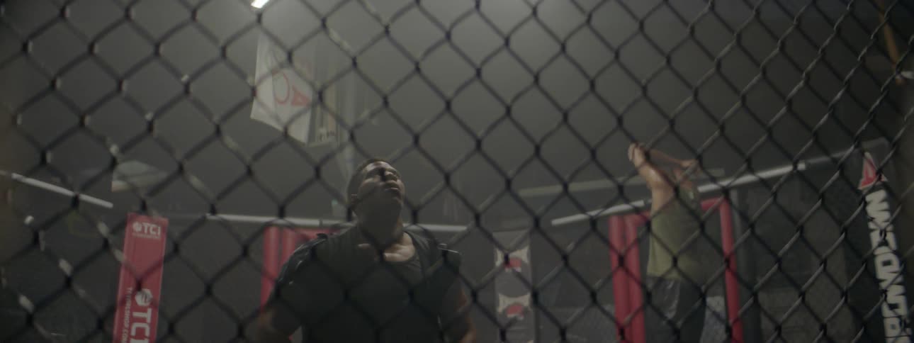 One main kneels while another man walks inside an mma ring